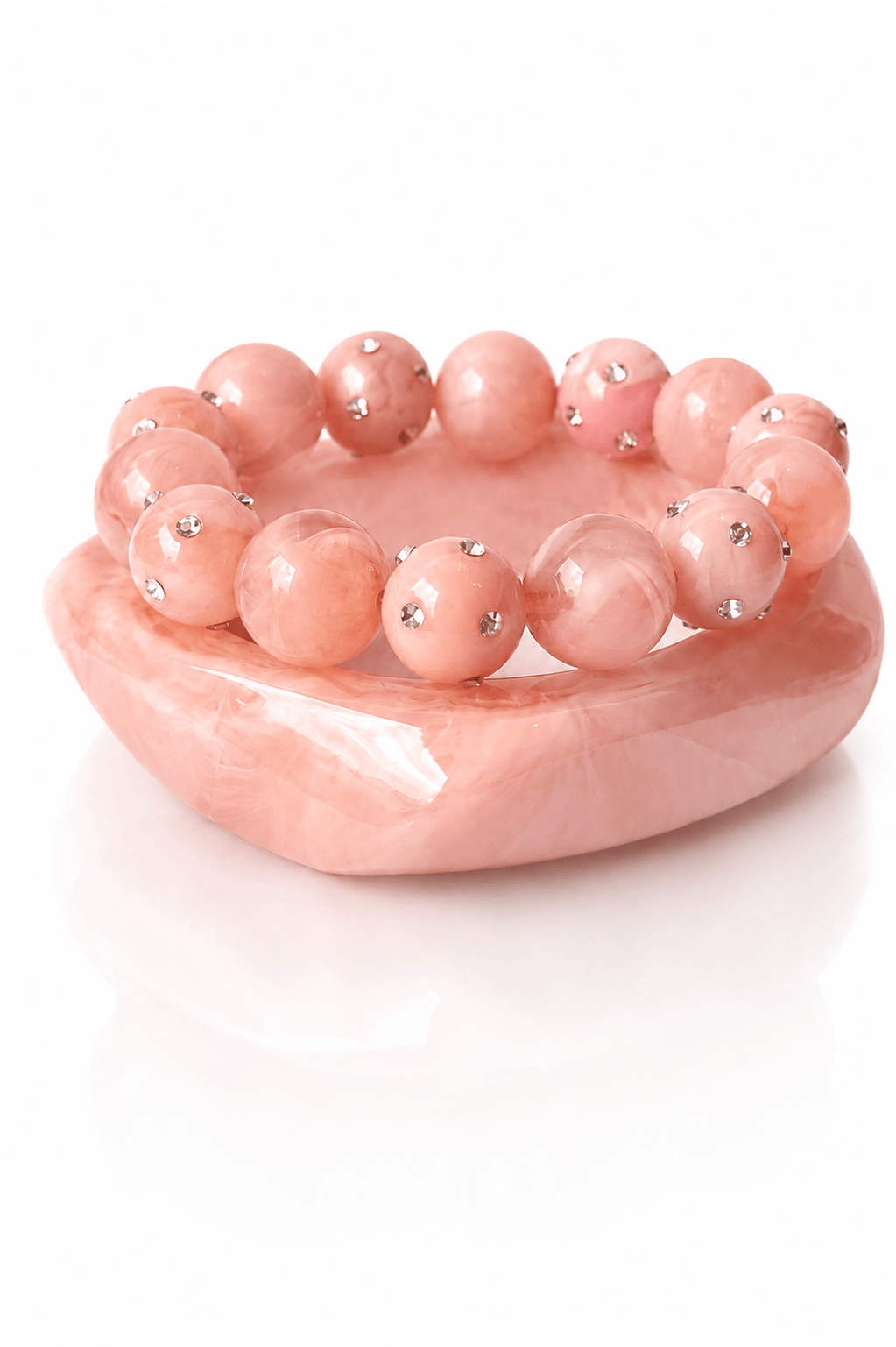 Marmorierter Resina-Armreif in Rosa mit passendem elastischen Perlenarmband in Rosatönen und kleinen Strassdetails auf weißem Hintergrund.
