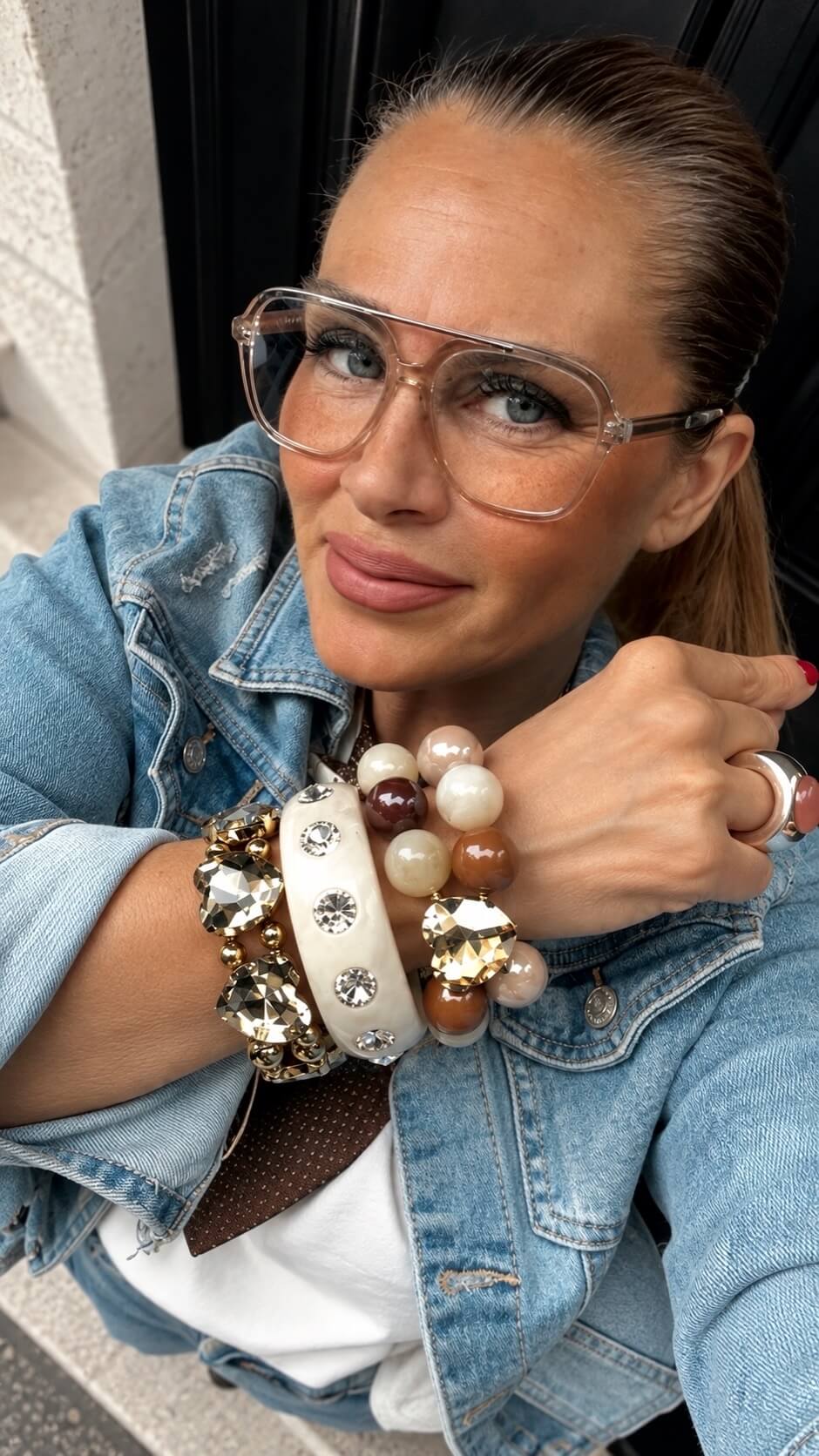 Frau in Jeansjacke trägt mehrere Crystal Hearts Armbänder von Casapari in Creme, Cognac und Gold am Handgelenk.