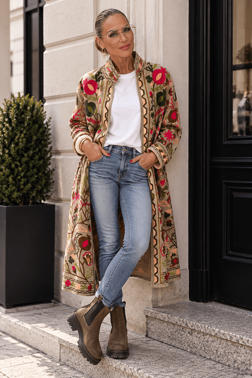 bestickter Casa Pari Samtmantel in Beige mit floralen Stickereien in Pink, Grün und warmen Naturtönen, getragen zu Jeans und Chelsea Boots.
