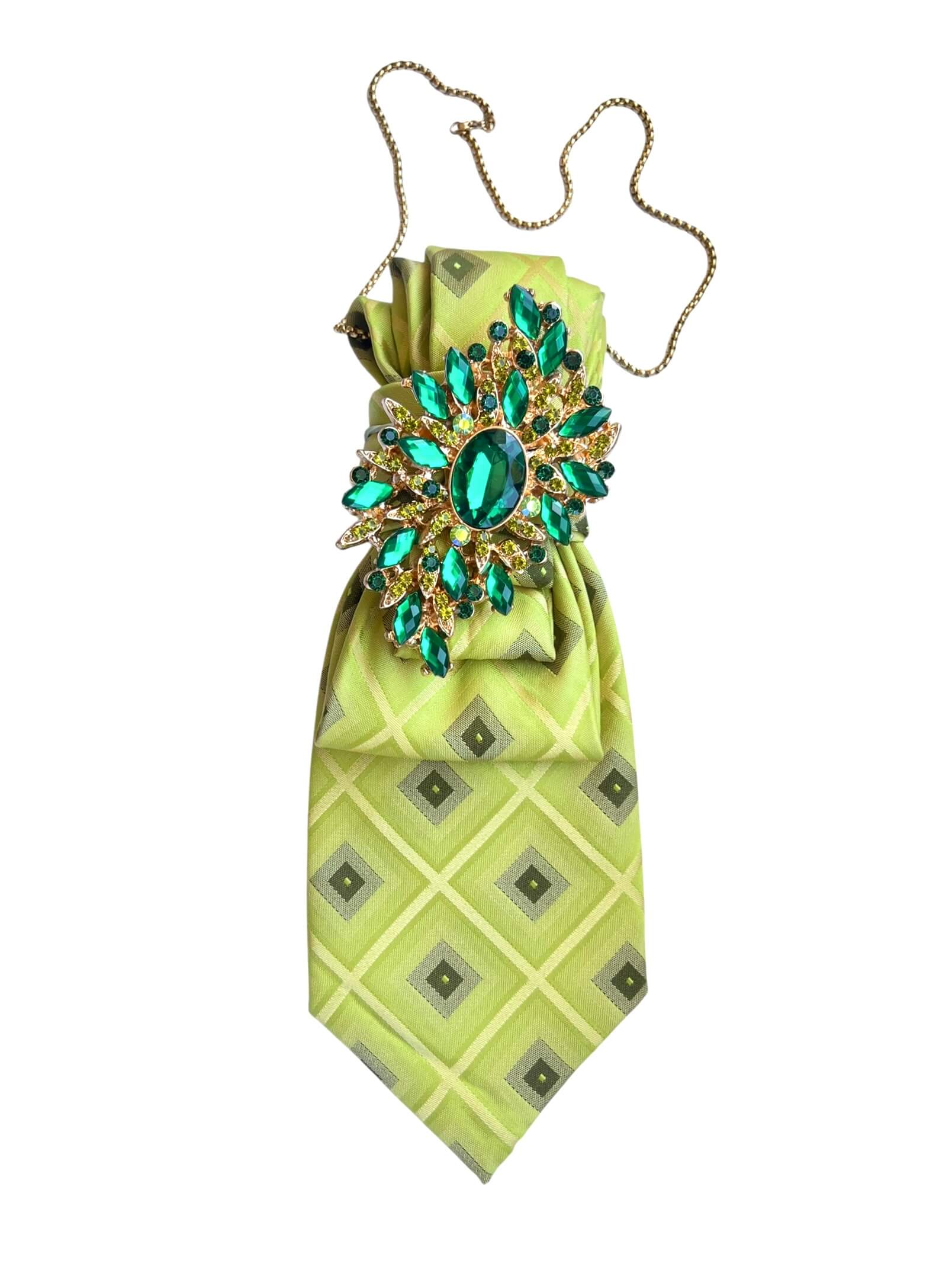 Seidenkrawatte in hellem Grün mit geometrischem Muster, kombiniert mit einer großen grünen Brosche und goldfarbener Kette, freigestellt auf hellem Hintergrund.