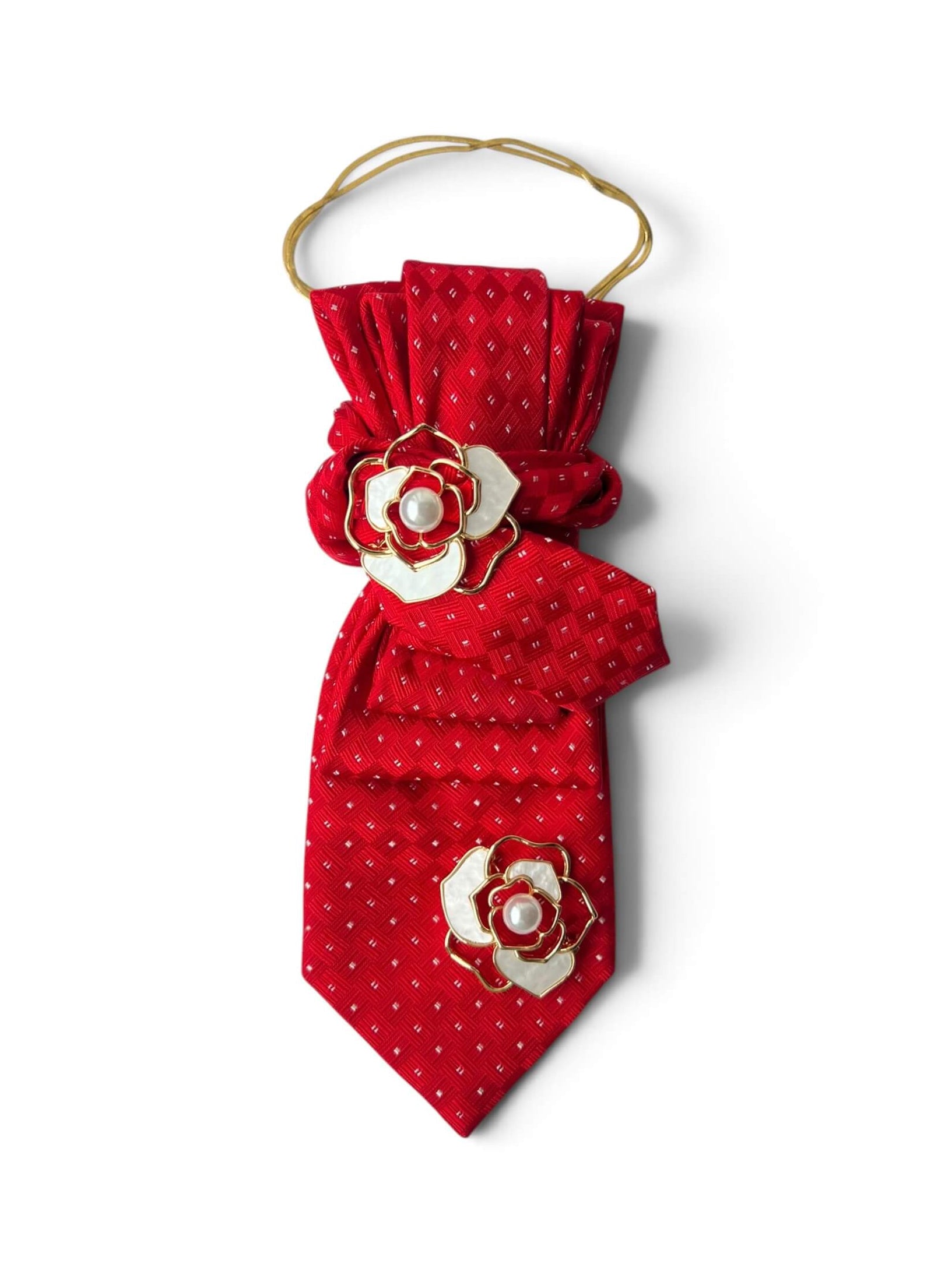 Leuchtend rote Vintage-Krawatte mit feinem Strukturmuster, verziert mit zwei weiß-roten Blütenbroschen mit Perlendetail und goldfarbener Kette.