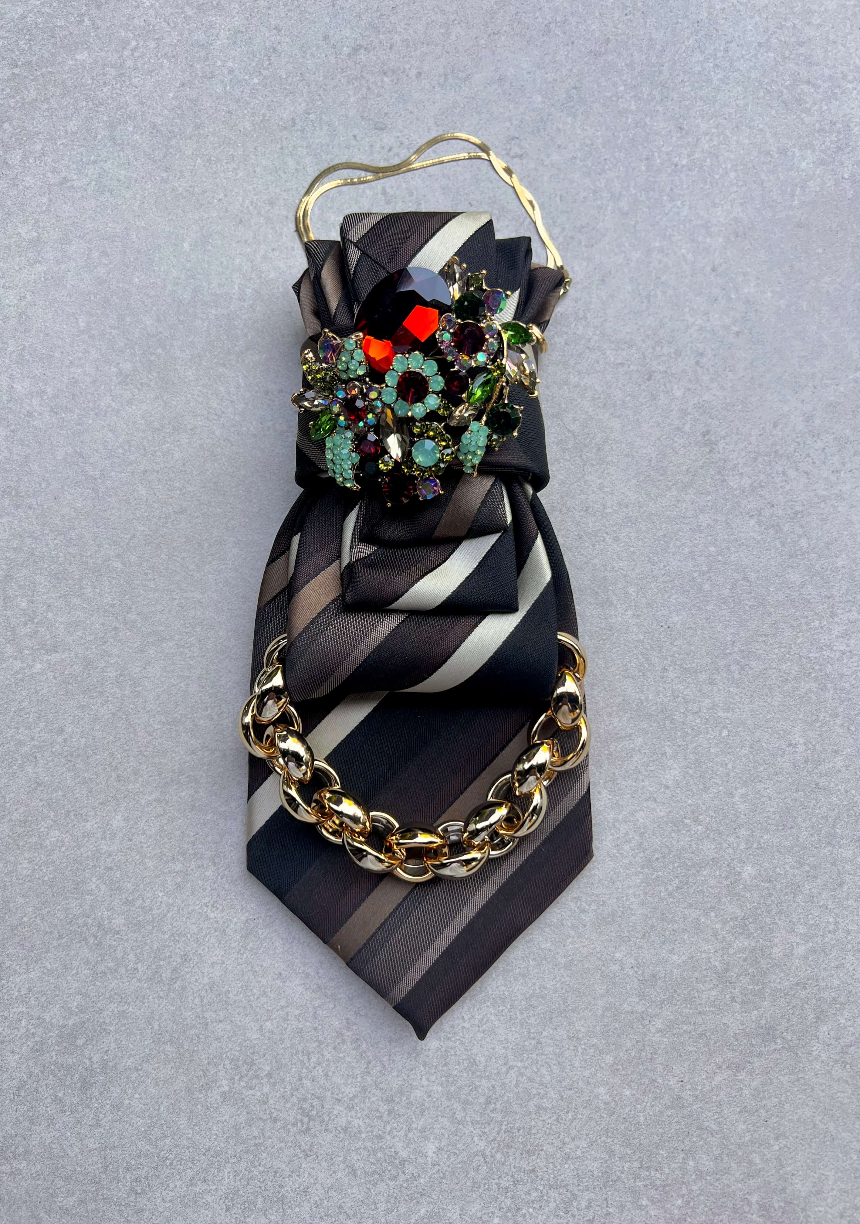 Dunkel gestreifter Krawatten-Schmuck von Casapari mit goldfarbener Halskette und großer Brosche aus mehrfarbigen Kristallsteinen in Blau, Türkis, Grün und Bordeaux.