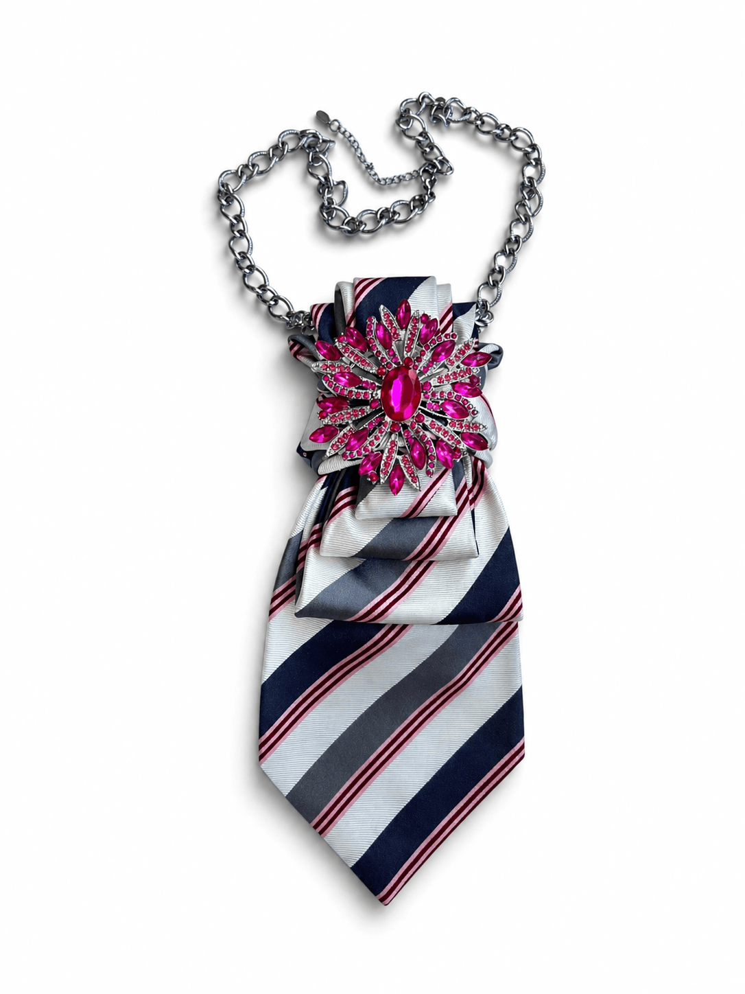 Seidenkrawatte mit diagonalem Streifenmuster in Navy, Weiß und Pink, dekoriert mit einer großen pinken Brosche und silberner Kette, auf hellem Hintergrund.