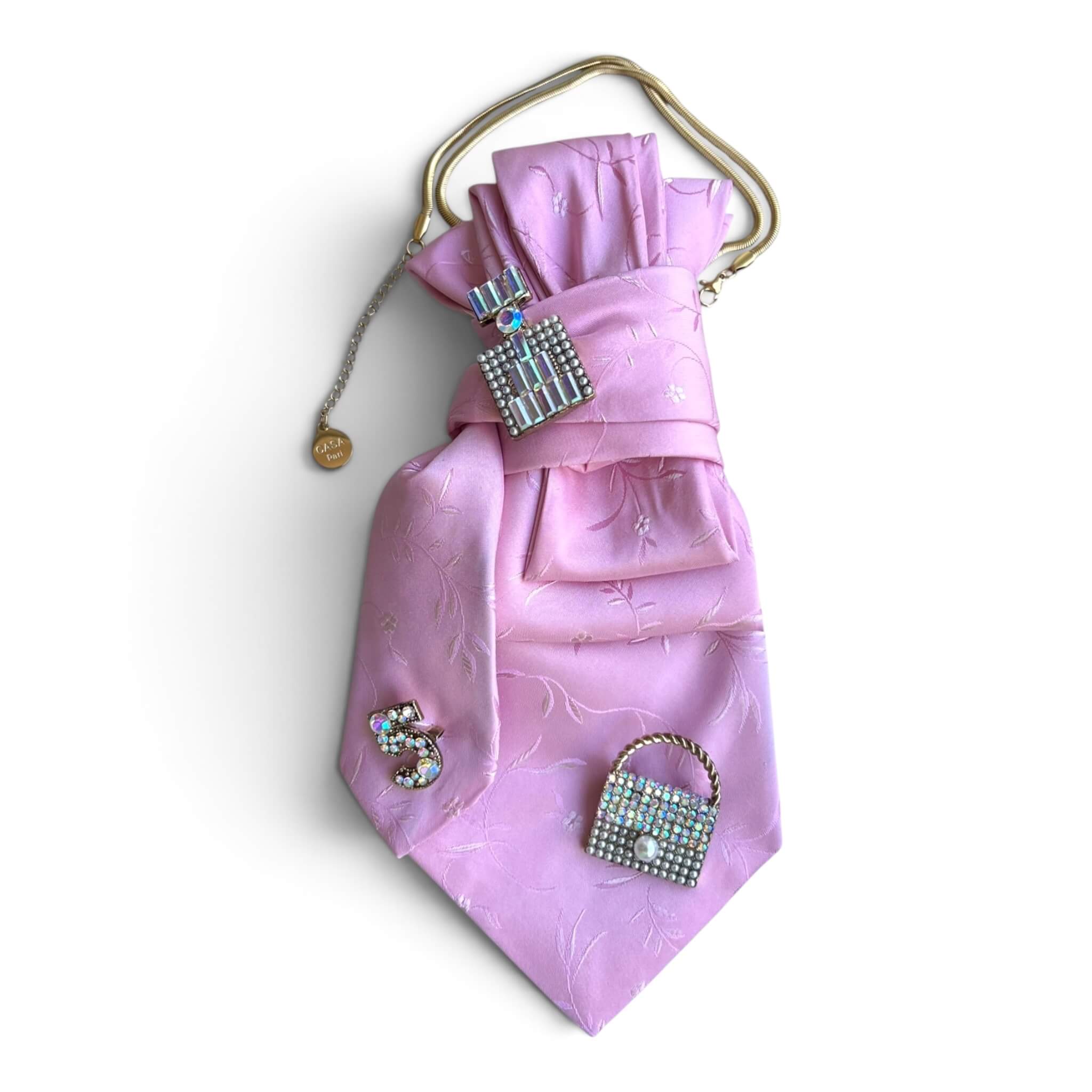 Rosafarbene CASAPARI Seidenkrawatte mit feinem Webmuster, goldfarbener Kette und funkelnden Schmuckbroschen in Handtaschen-Optik.