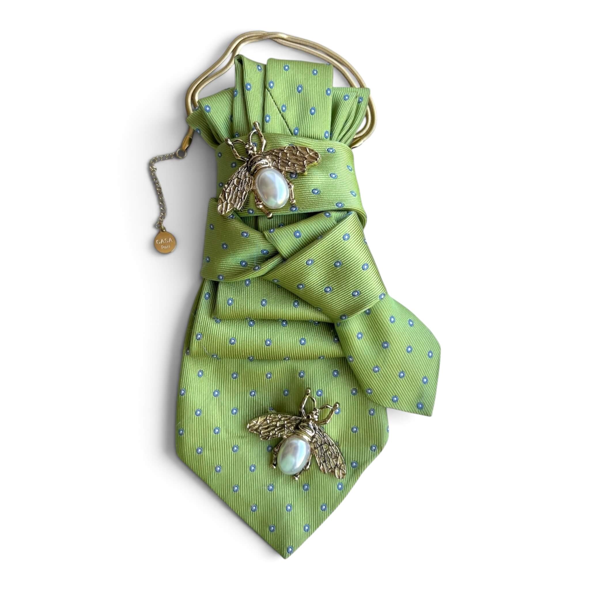 Grüne CASAPARI Seidenkrawatte mit blauen Punkten, goldfarbener Kette und zwei Bienenbroschen mit Perlmutt.