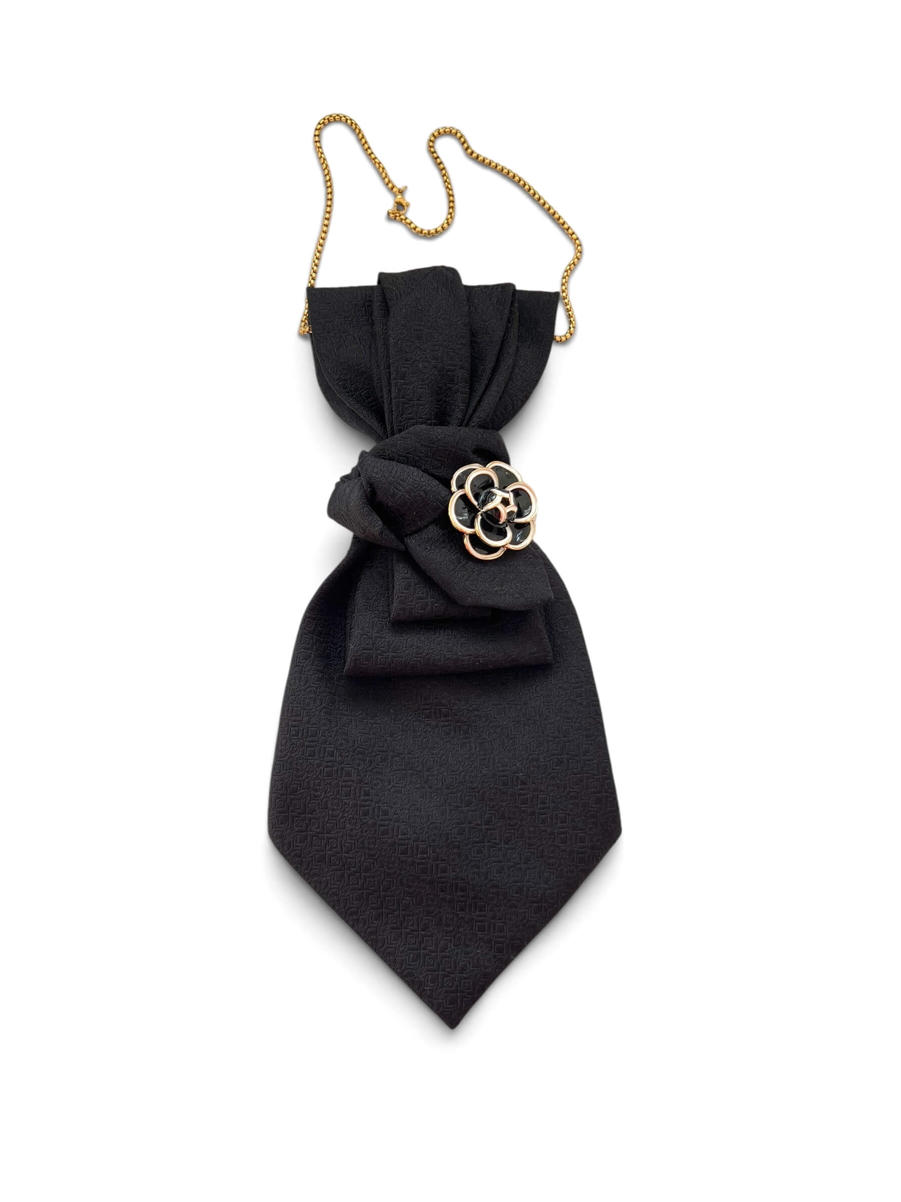 Schwarze Krawatte mit Strukturmuster, goldfarbener Kette und schwarzer, floraler Brosche mit goldenen Details.
