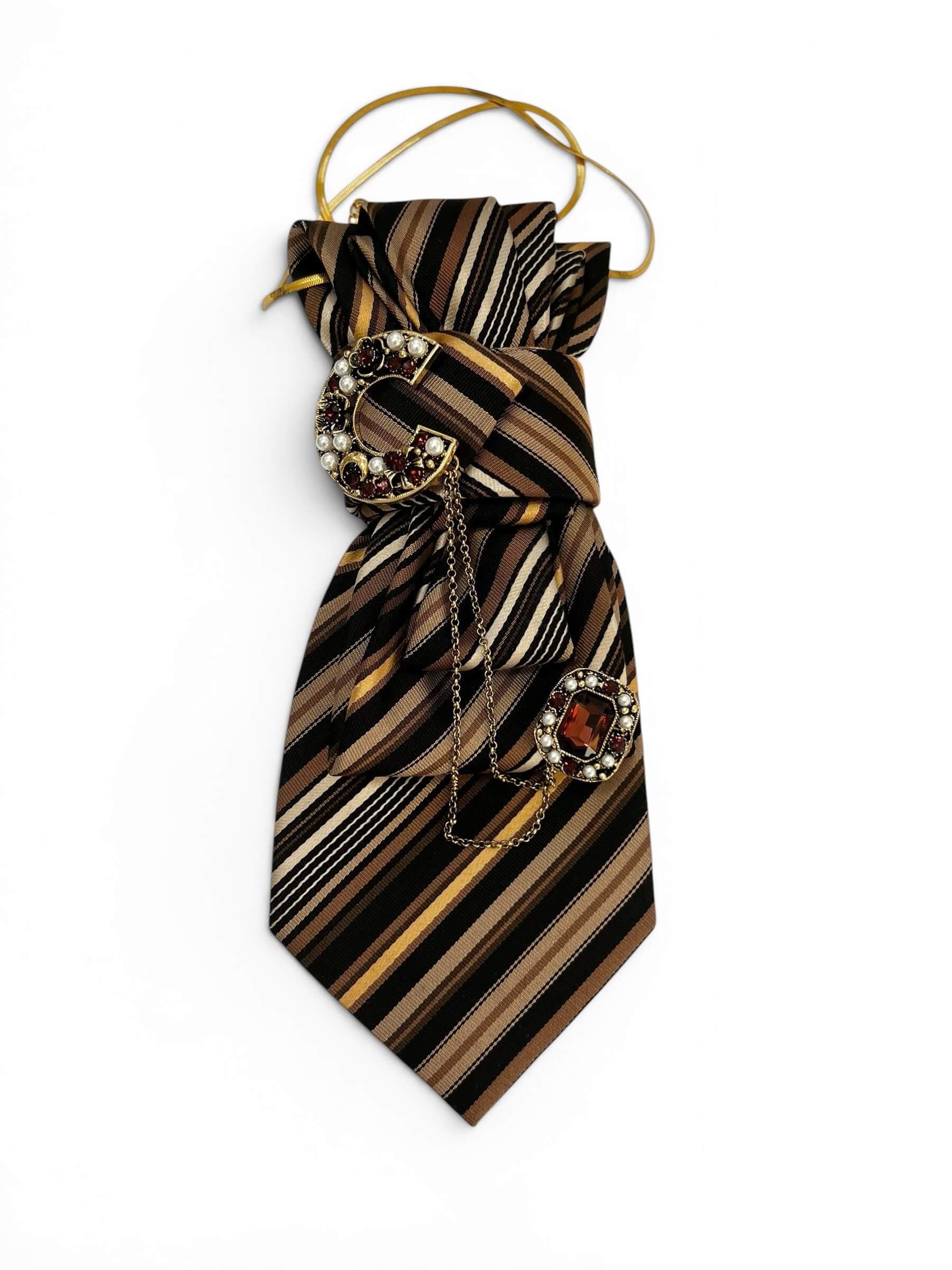 Vintage-Bindekrawatte mit Streifenmuster in Schwarz, Mocha, Beige und Gold, dekoriert mit einer goldfarbenen Schmuckbrosche mit dunklen roten Steinen und Perlendetails.