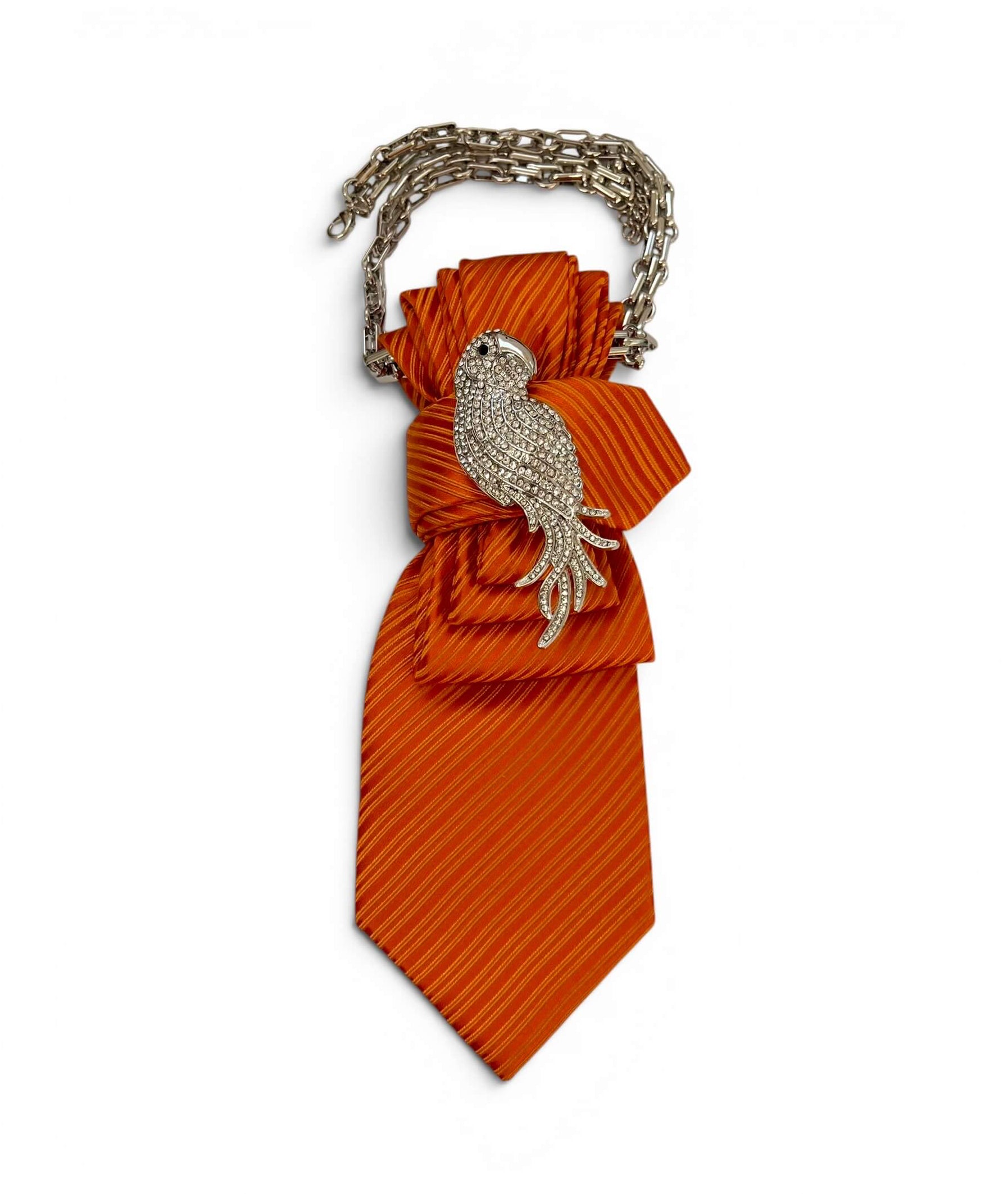 Orange gestreifte Krawatte mit silberfarbener Vogelbrosche und Kette auf hellem Hintergrund.