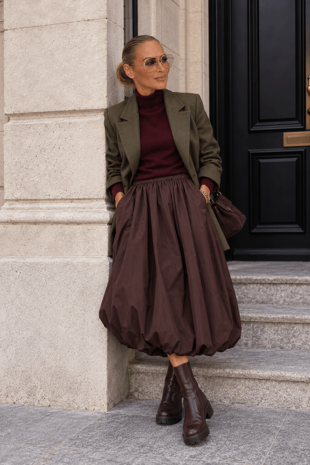 Frau trägt einen schokoladenbraunen Ballonrock mit burgundyfarbenem Rollkragenpullover, olivgrünem Blazer und braunen Chelsea Boots.