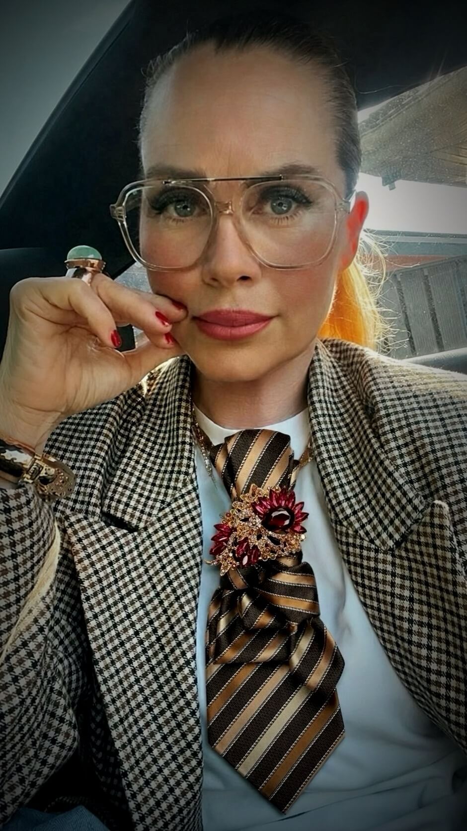 Frau trägt weißes Oberteil mit kariertem Blazer und eine braun-gold gestreifte Vintage-Krawatte mit großer bordeauxfarbener Schmuckbrosche.