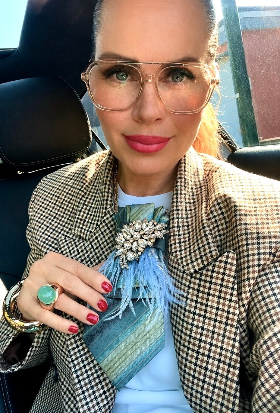 Model trägt eine Vintage-Krawatte in Blau-, Türkis- und Salbeitönen mit silberfarbener Kristallbrosche und hellblauen Federn, kombiniert mit kariertem Blazer und weißem Oberteil.