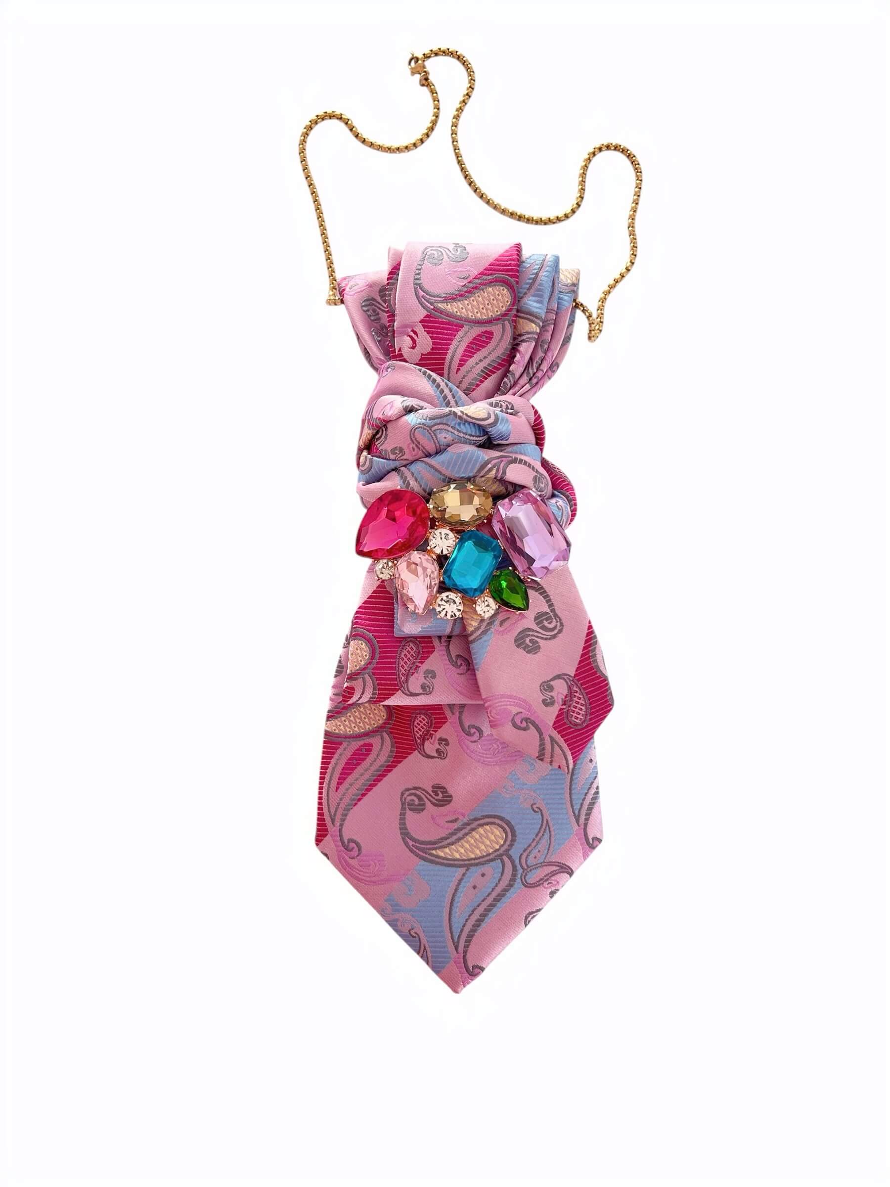 Rosafarbene Vintage-Krawatte mit Paisley-Muster, gebunden dargestellt, verziert mit einer Brosche aus bunten Steinen und goldfarbener Kette vor hellem Hintergrund.