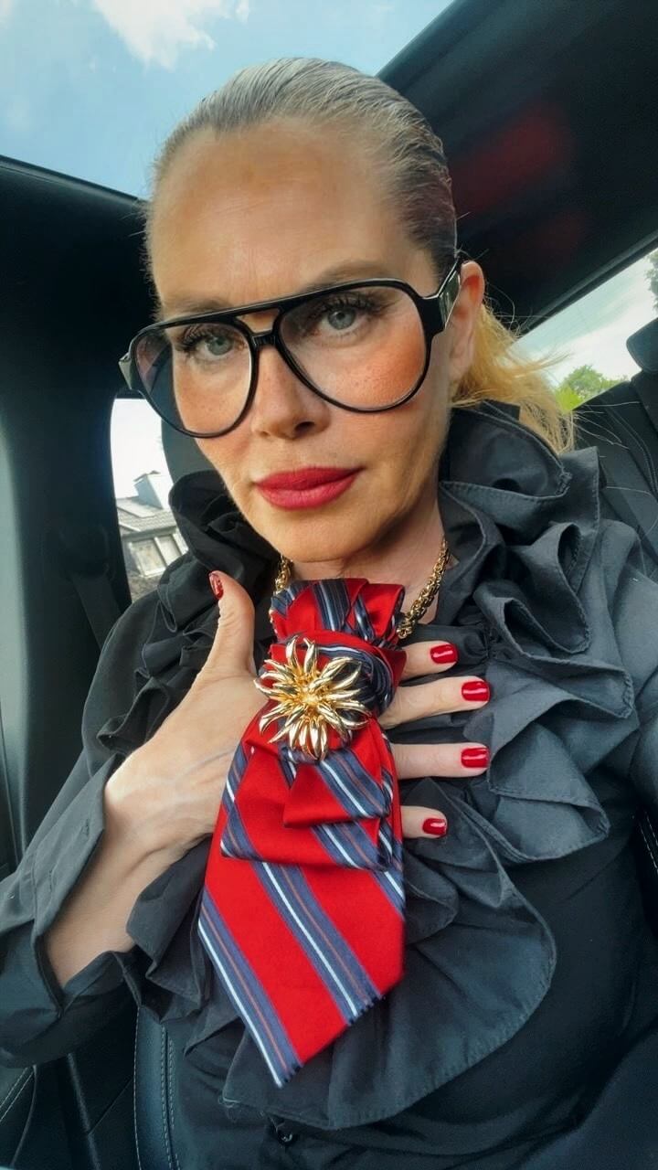 Frau trägt eine rote gestreifte Vintage-Krawatte mit goldfarbener Brosche als Statement-Accessoire zu dunkler Bluse.