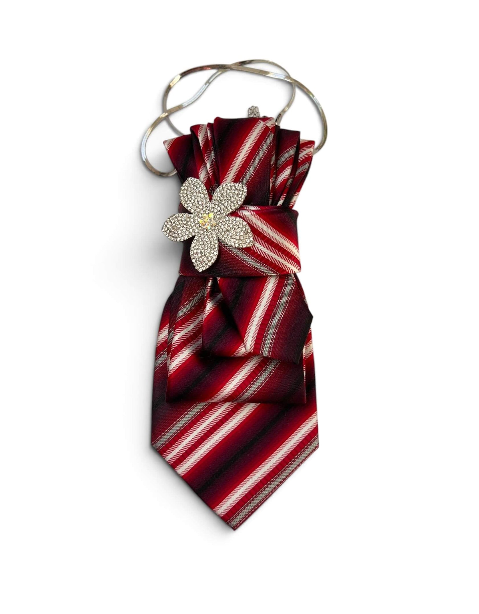 Vintage-Krawatte in Rot mit diagonalen Streifen in Bordeaux, Creme und Schwarz, dekorativer glitzernder Blumenbrosche und silberfarbener Kette auf hellem Hintergrund.