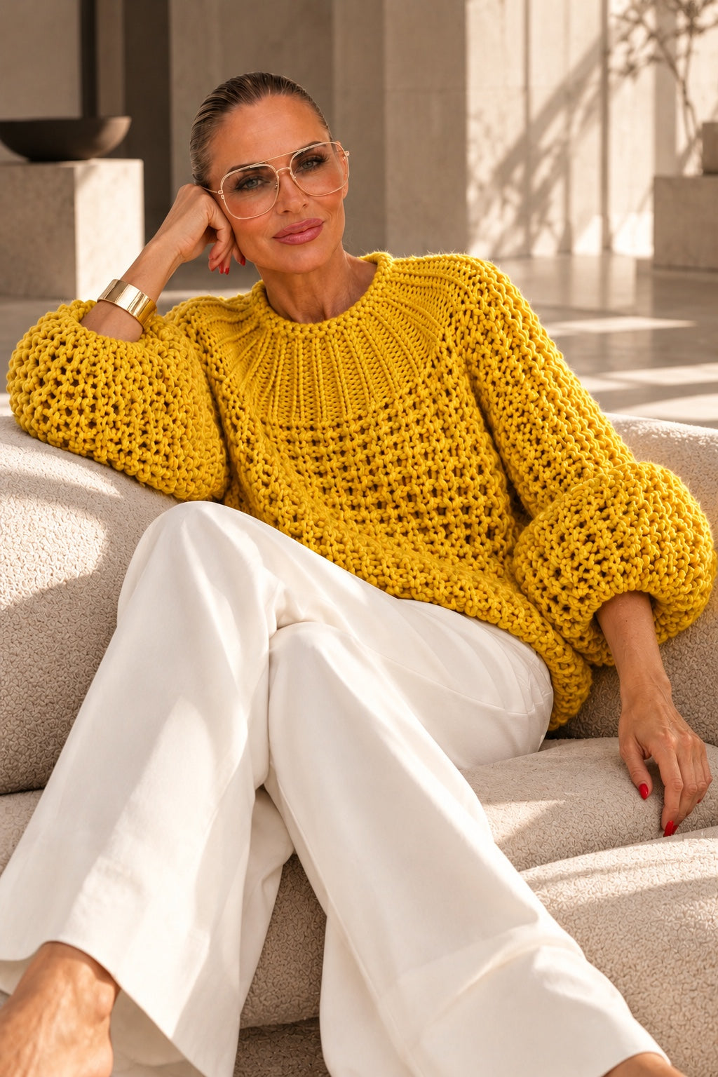 Model im ockergelben Chunky-Knit-Grobstrickpullover mit weißer Marlenehose, rote Fingernägel