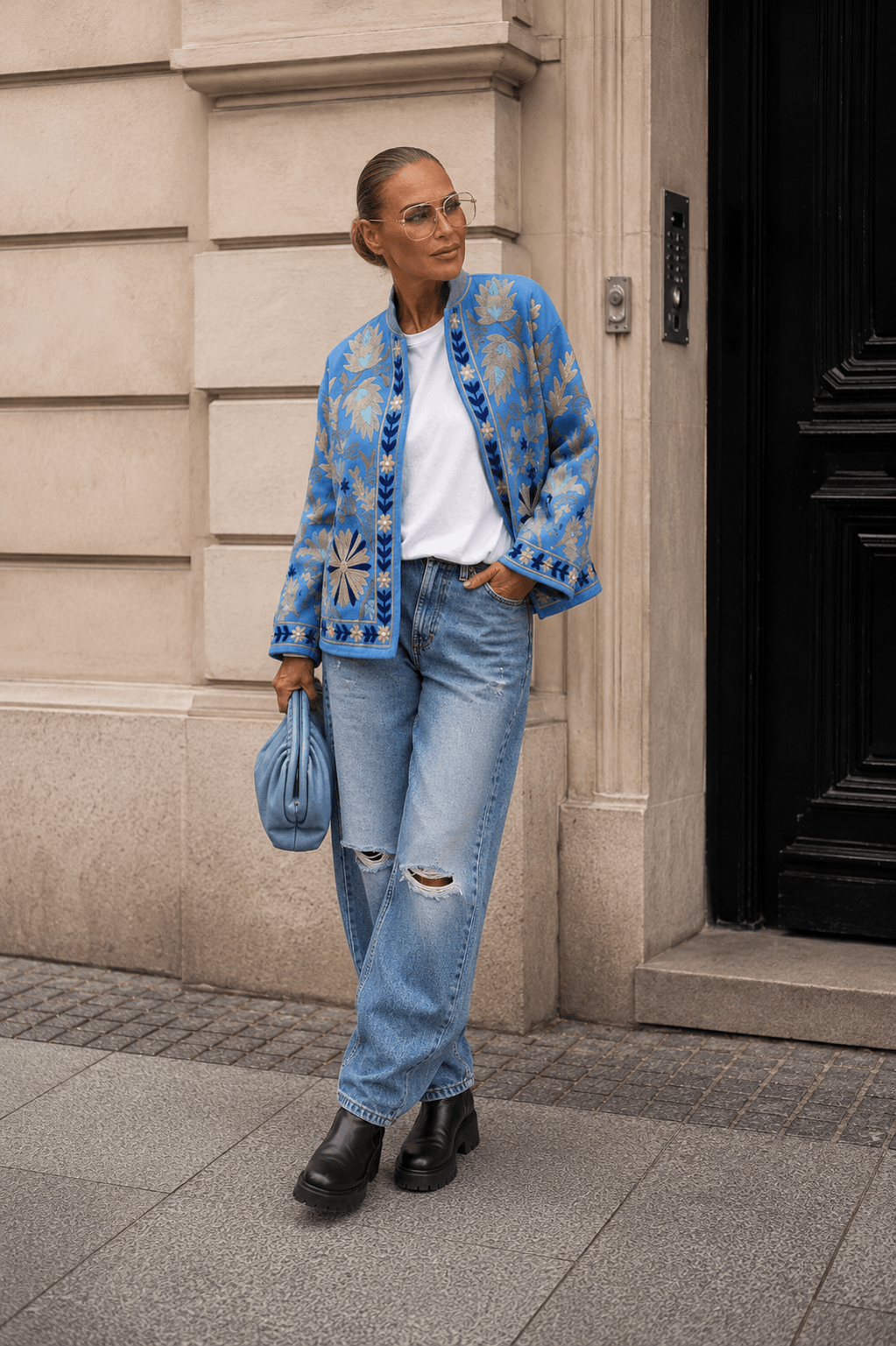 frau steht auf Straße hat jeans hose an. Blaue Blumenjacke und hält eine Tasche in der Hand