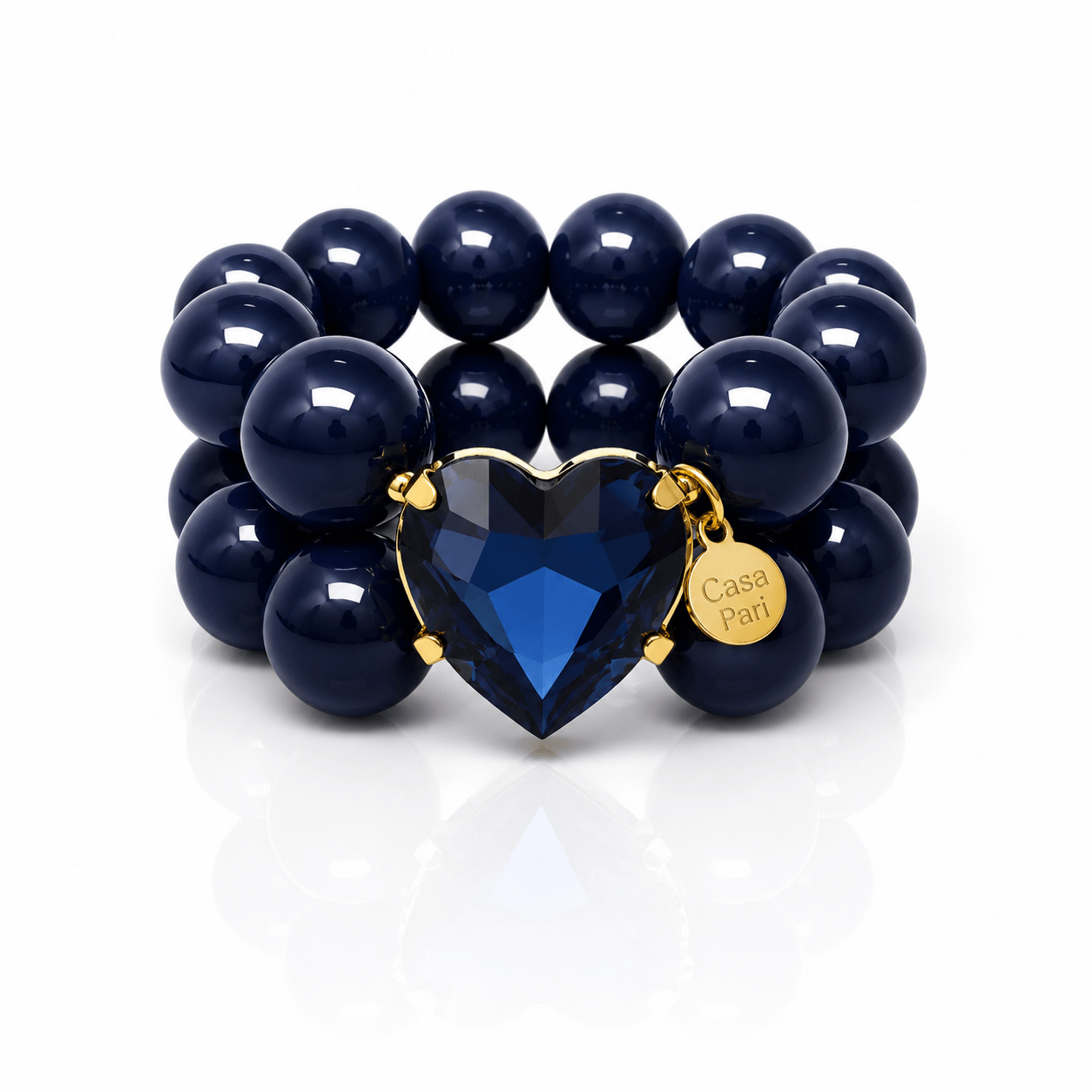 Crystal Heart Armband mit glänzenden schwarzen Perlen und großem herzförmigem Anhänger in Saphirblau mit goldfarbener Fassung auf hellem Hintergrund.