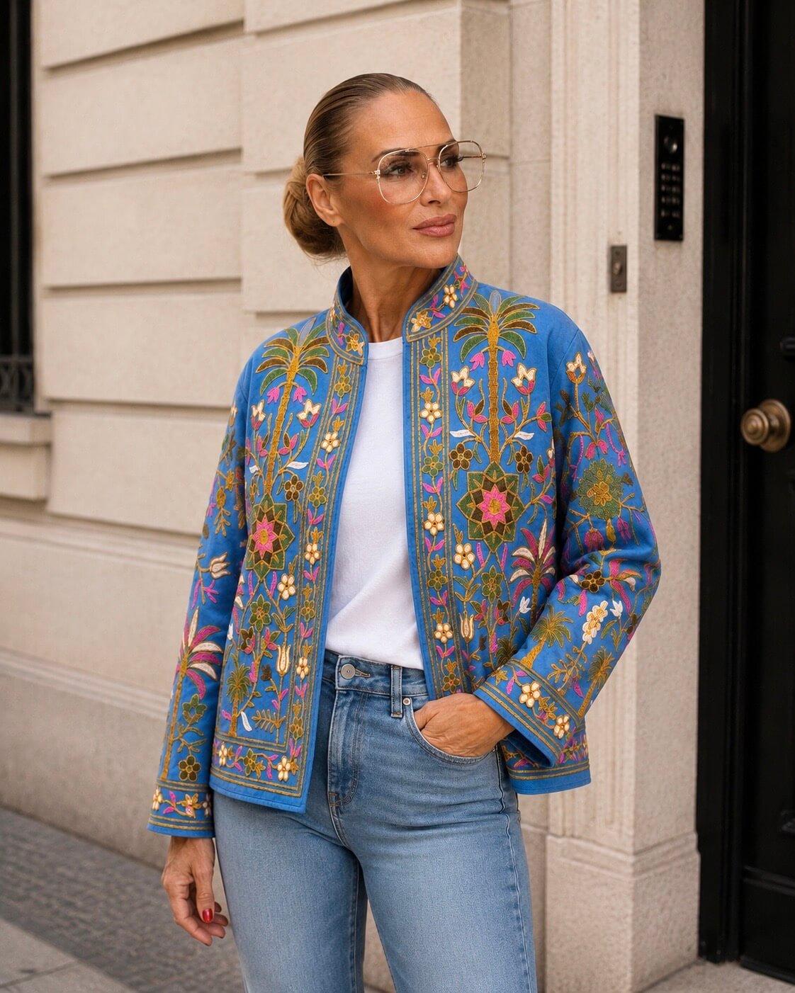 Blaue bestickte Damenjacke mit farbenfrohen Blumen- und Palmenmotiven, getragen mit weißem Shirt und Jeans.