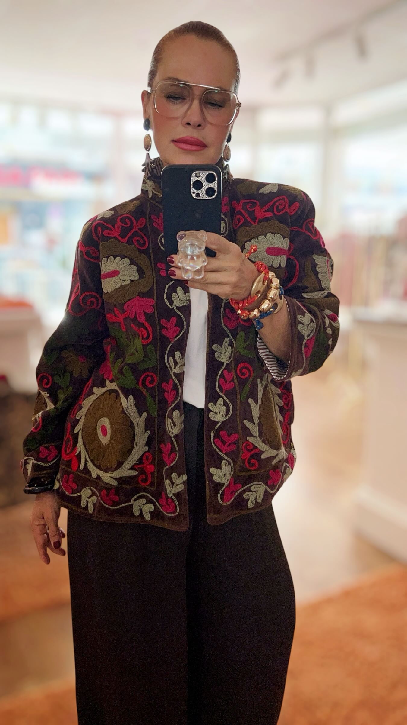 Braune Embroidery-Jacke mit floralen Stickereien in Creme, Olivgrün und Himbeerrot, offen getragen über einem weißen Oberteil.