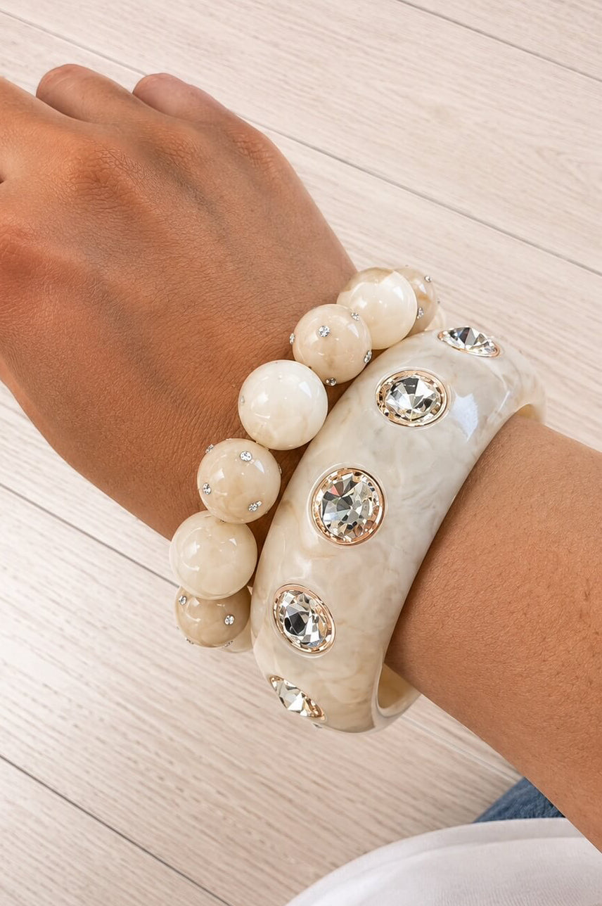 Cremefarbenes Schmuckset aus Perlenarmband und Armreif mit Kristallsteinen am Handgelenk getragen.