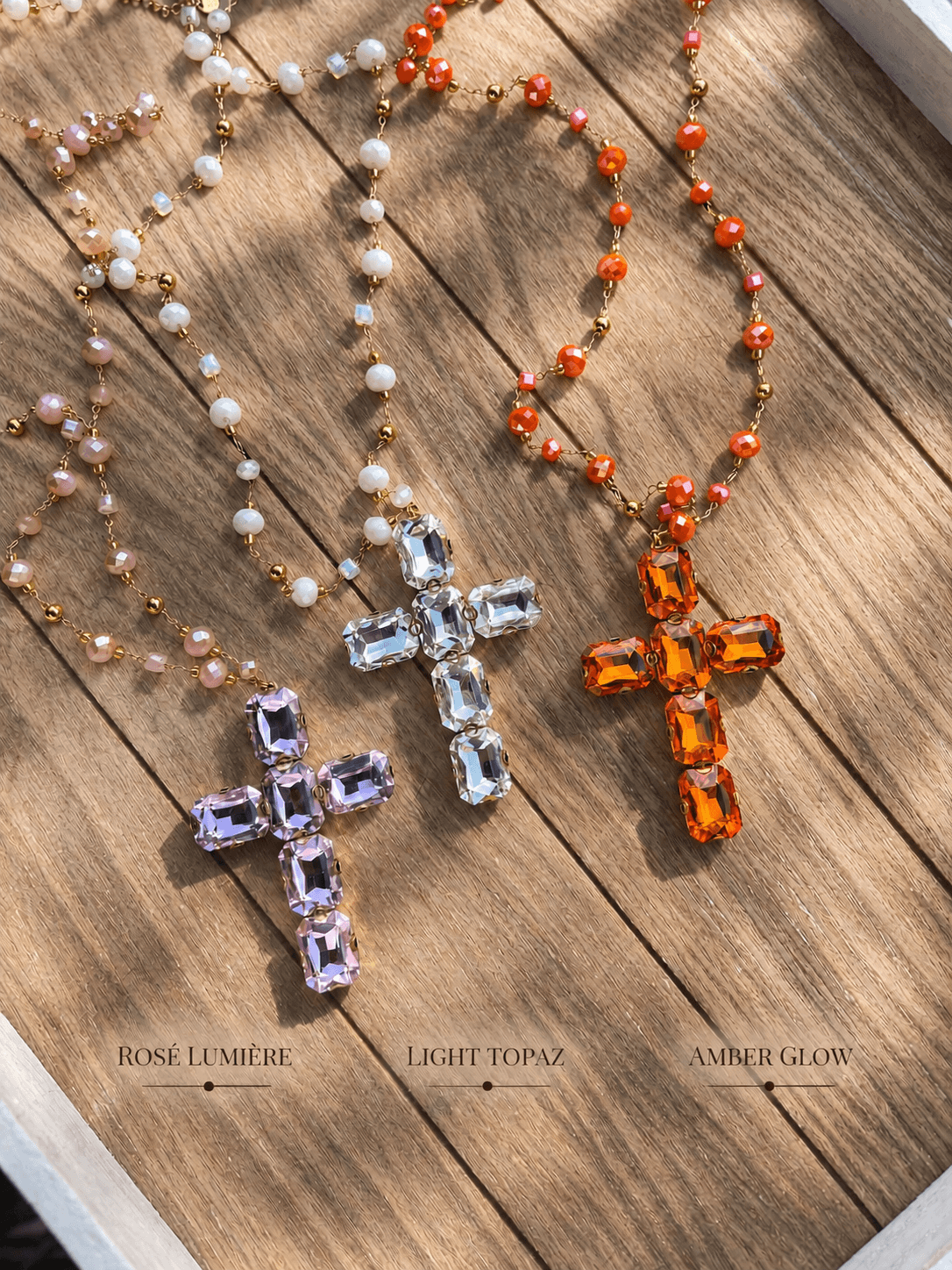 drei Kreuzketten in rosa topaz und amber liegen auf einem Holzbrett