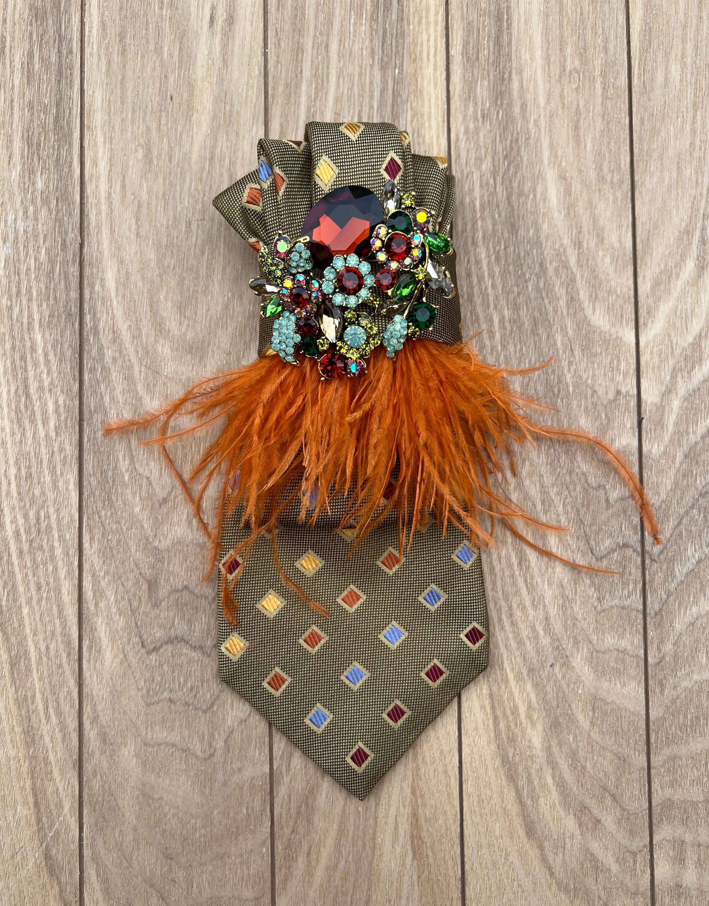 Taupefarbene Statement-Krawatte mit geometrischem Muster, orangefarbenen Federn und funkelnder Schmuckbrosche.