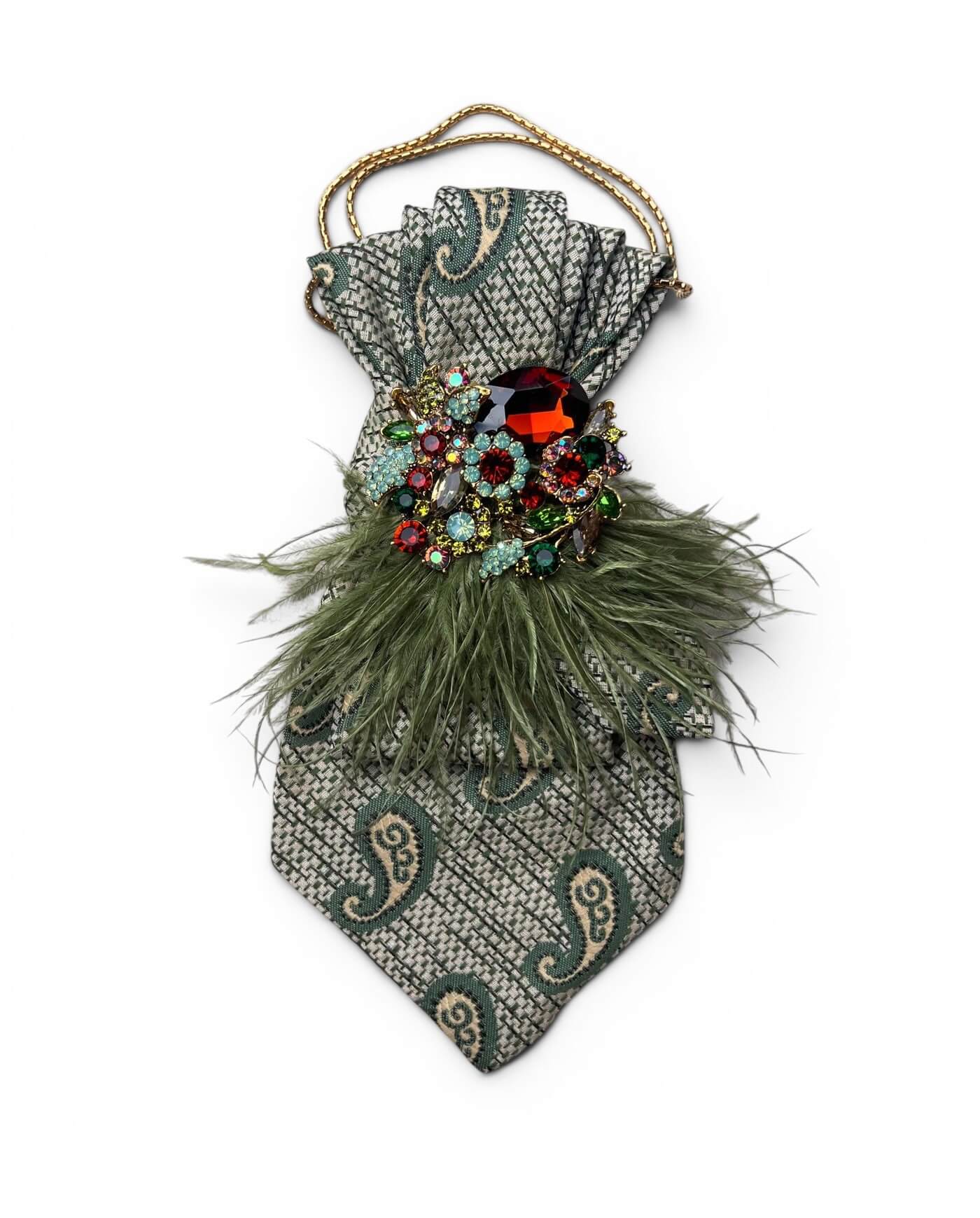 Salbeigrüne Krawatte mit Paisley-Muster, mehrfarbiger Schmuckbrosche, grünen Federn und goldfarbener Kette auf neutralem Hintergrund.