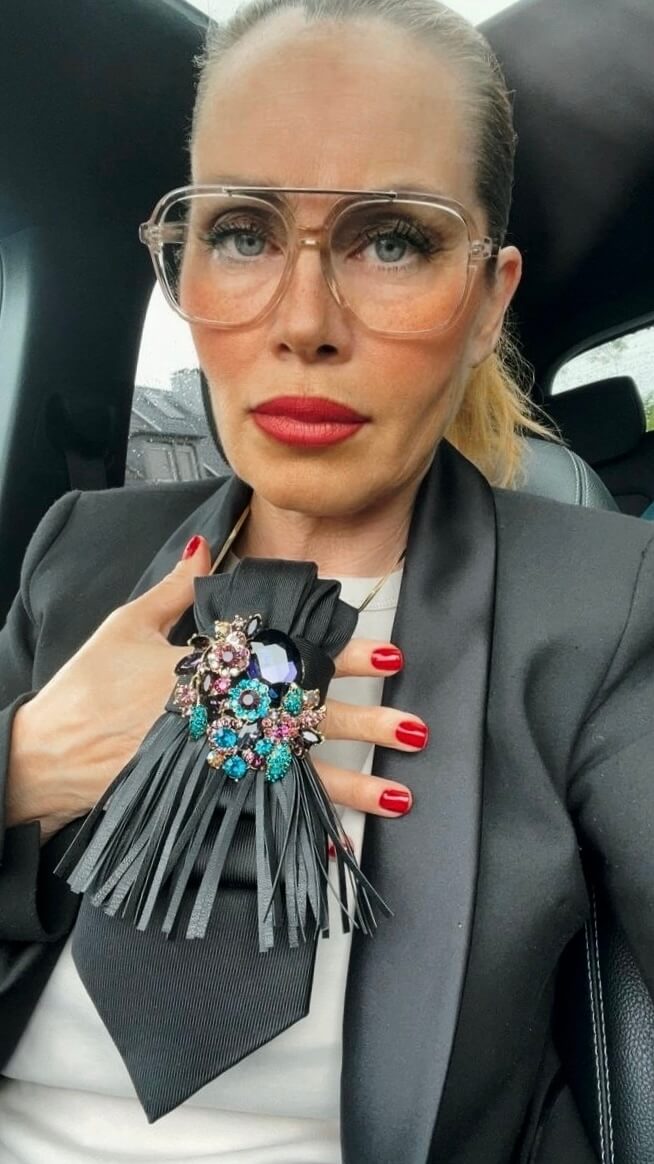 Detailansicht einer schwarzen Vintage-Krawatte mit dekorativer Brosche und Fransen-Detail, getragen mit schwarzem Blazer.