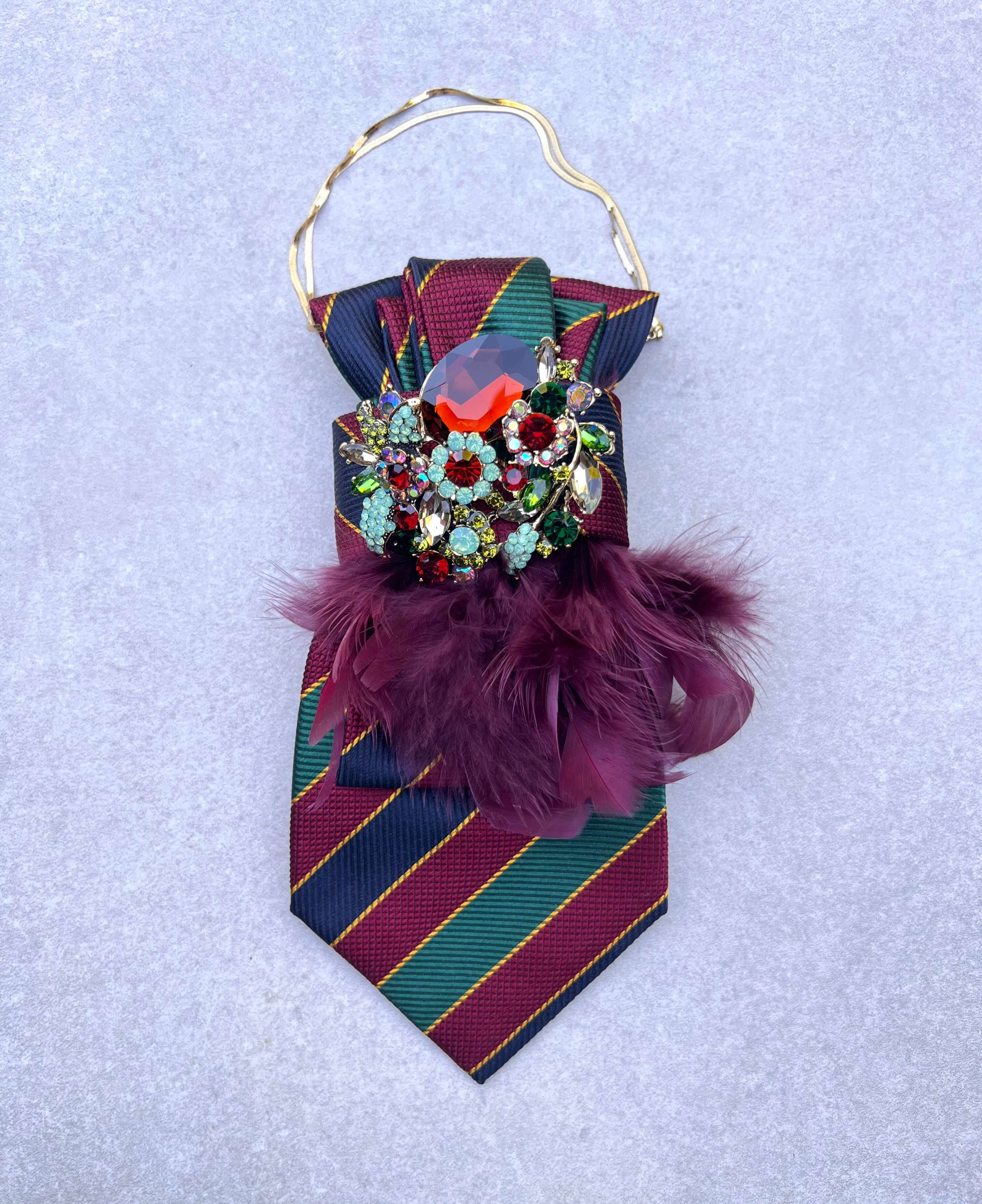 Gestreifte Feather-Affair-Krawatte in Bordeaux, Dunkelblau und Grün mit goldfarbener Kette, funkelnder Kristallbrosche in Rot, Grün und Türkis sowie bordeauxfarbenen Federn.