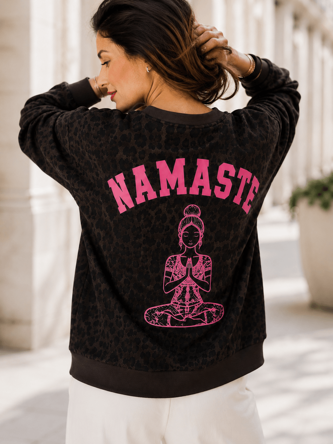 Frau von hinten im schokobraunen Leo-Sweatshirt mit großem pinkfarbenem Namaste-Print und Yoga-Motiv auf dem Rücken.