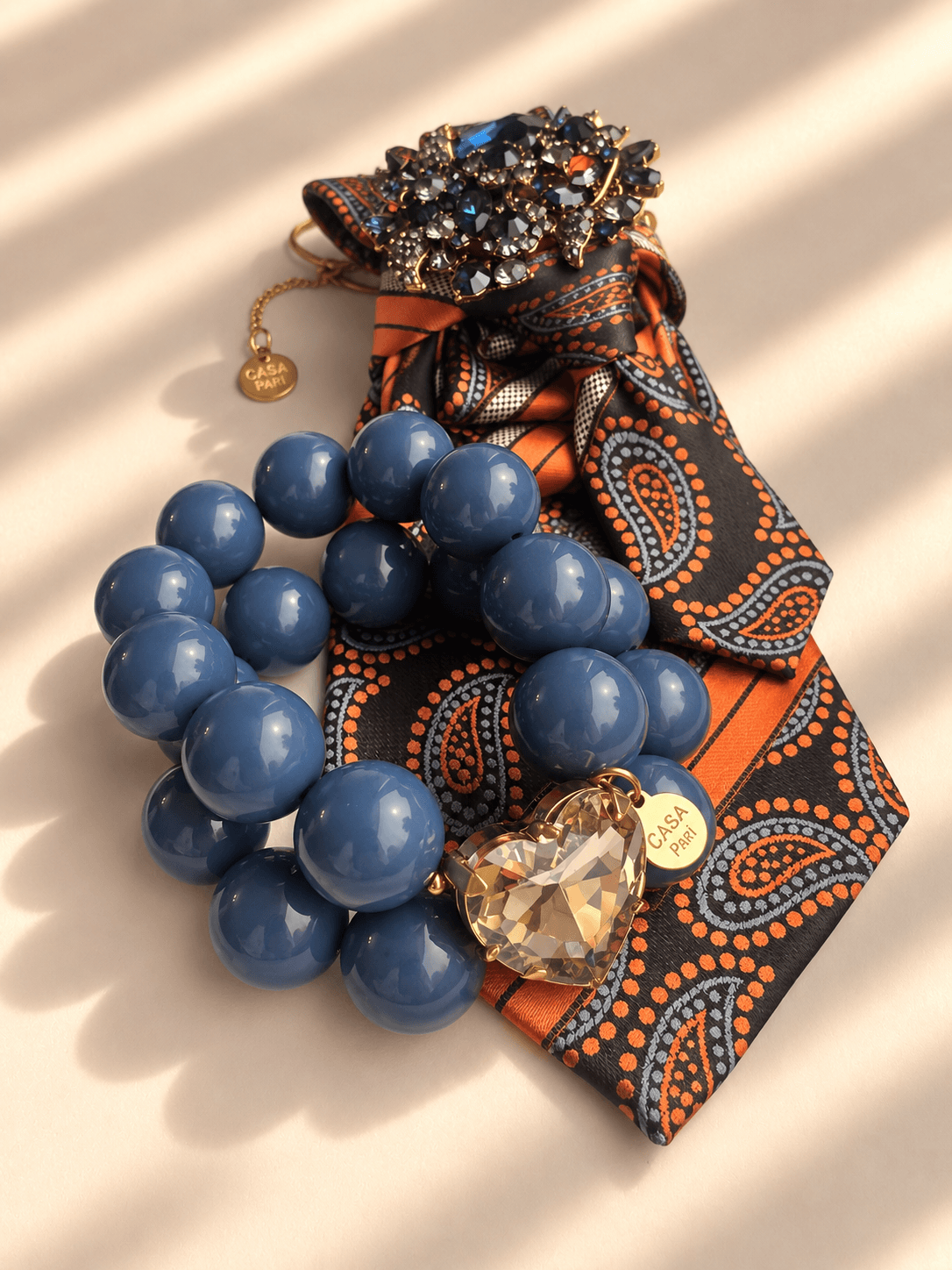 Casa Pari Crystal Heart Armband Denim Smoke kombiniert mit orange-brauner Paisley-Krawatte und Schmuckdetail