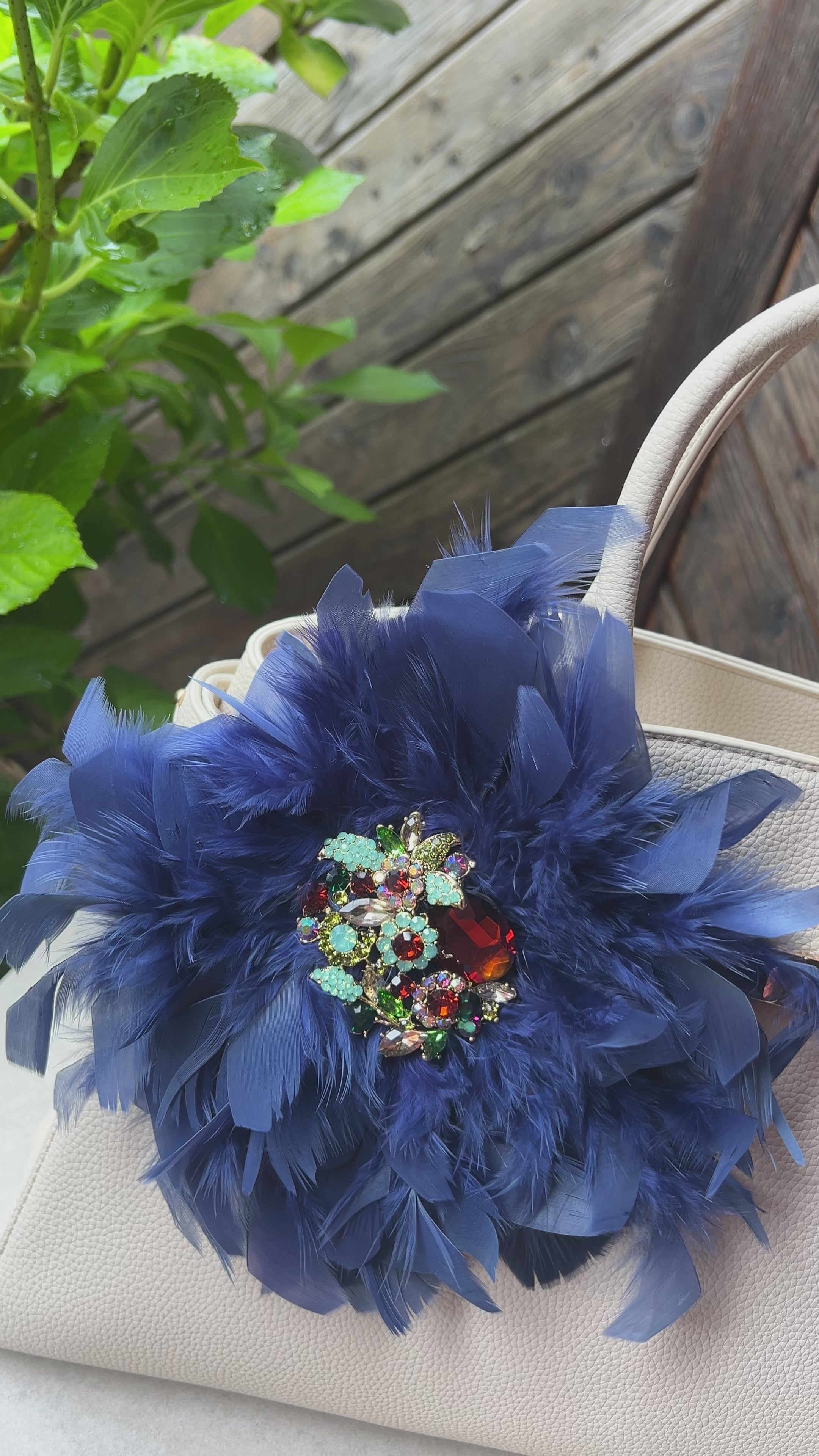 Blaue Brosche mit Schmuckelement an einer Beigen Tasche drapiert. Hinter einer Holzwand