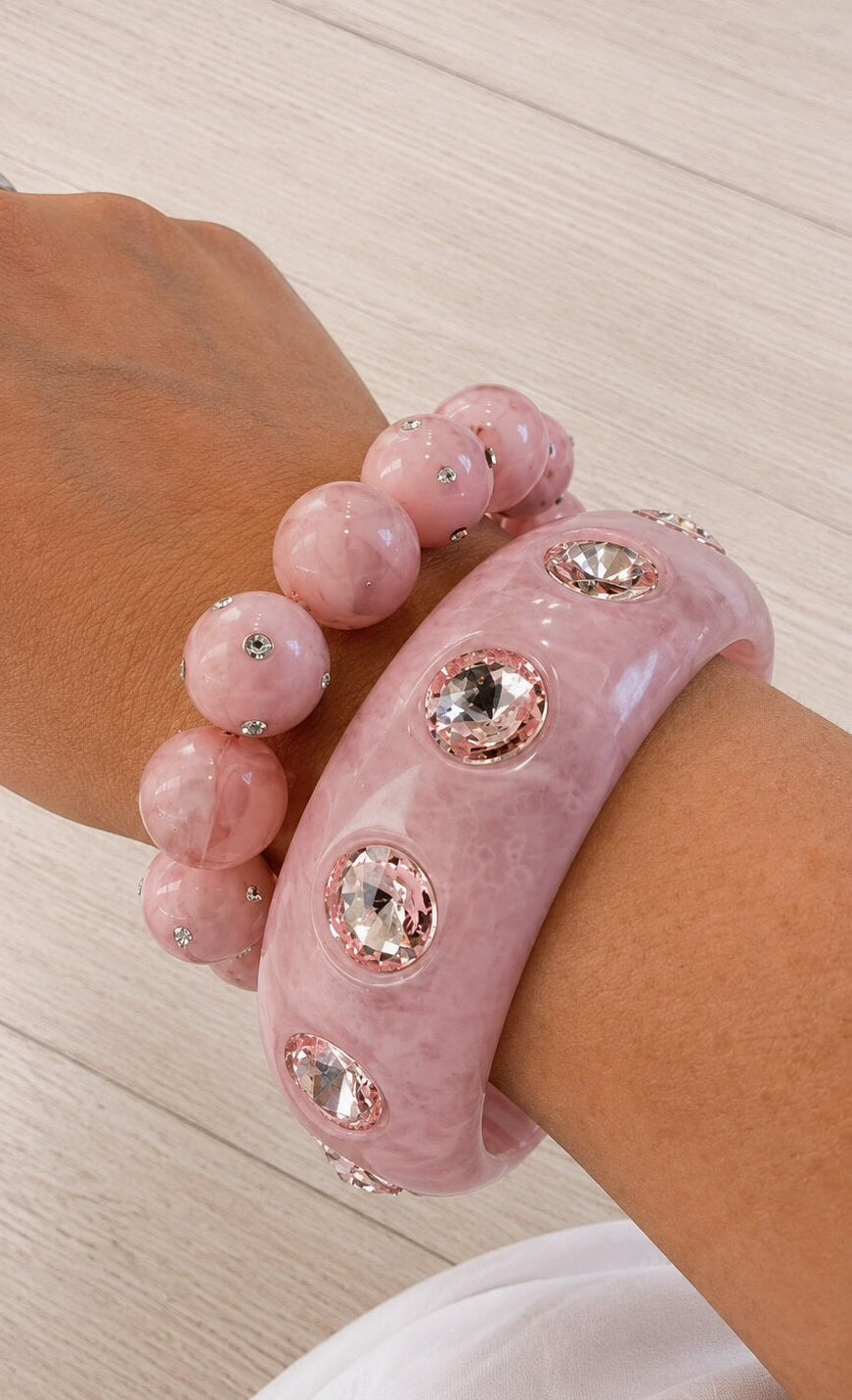 Rosafarbener Armreif mit facettierten Kristallsteinen kombiniert mit einem passenden Perlenarmband in Rosé auf einem Handgelenk getragen.