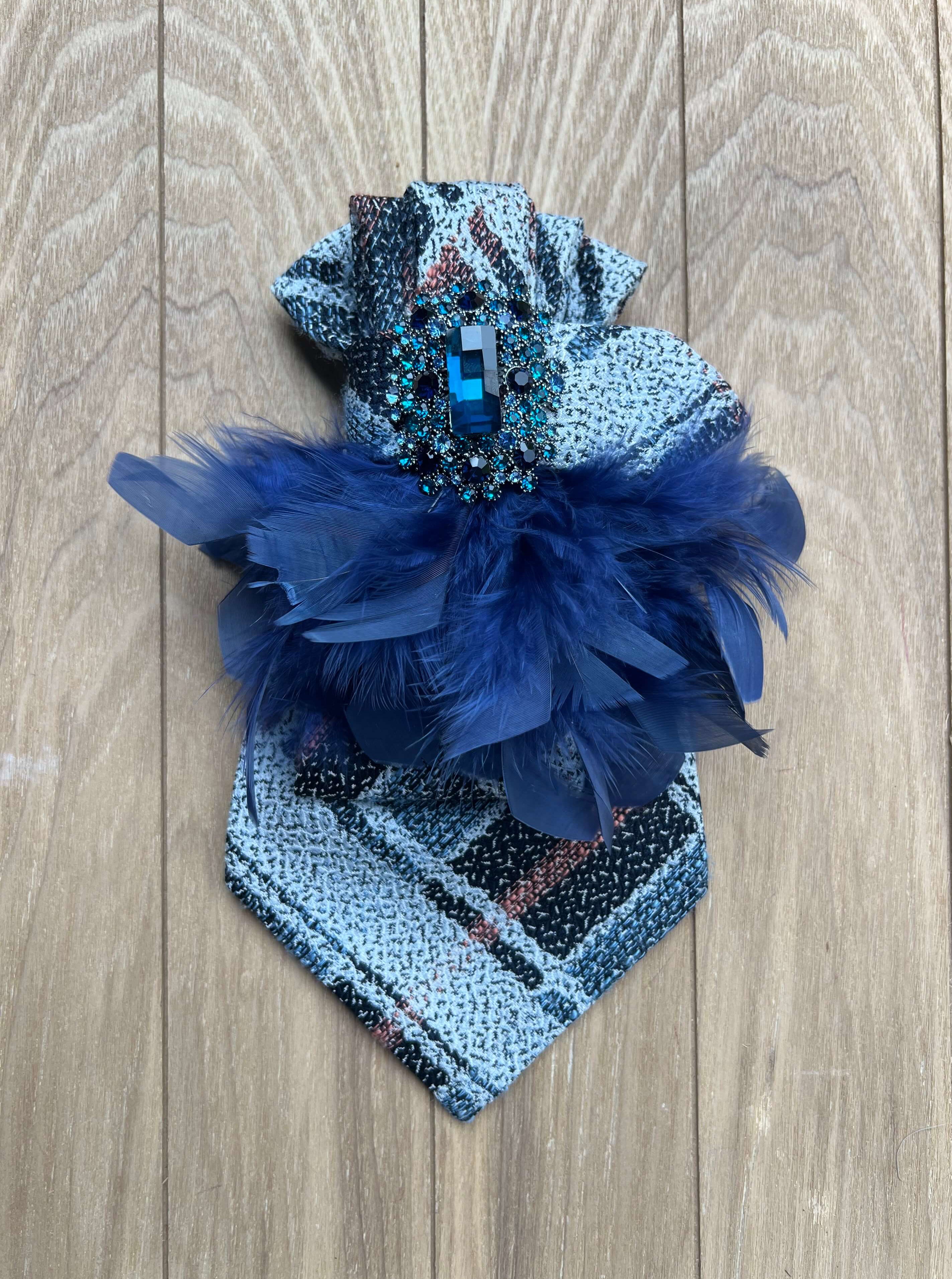 Blaue Vintage-Seidenkrawatte mit Schmuckbrosche und dunkelblauen Federn auf hellem Holzhintergrund.