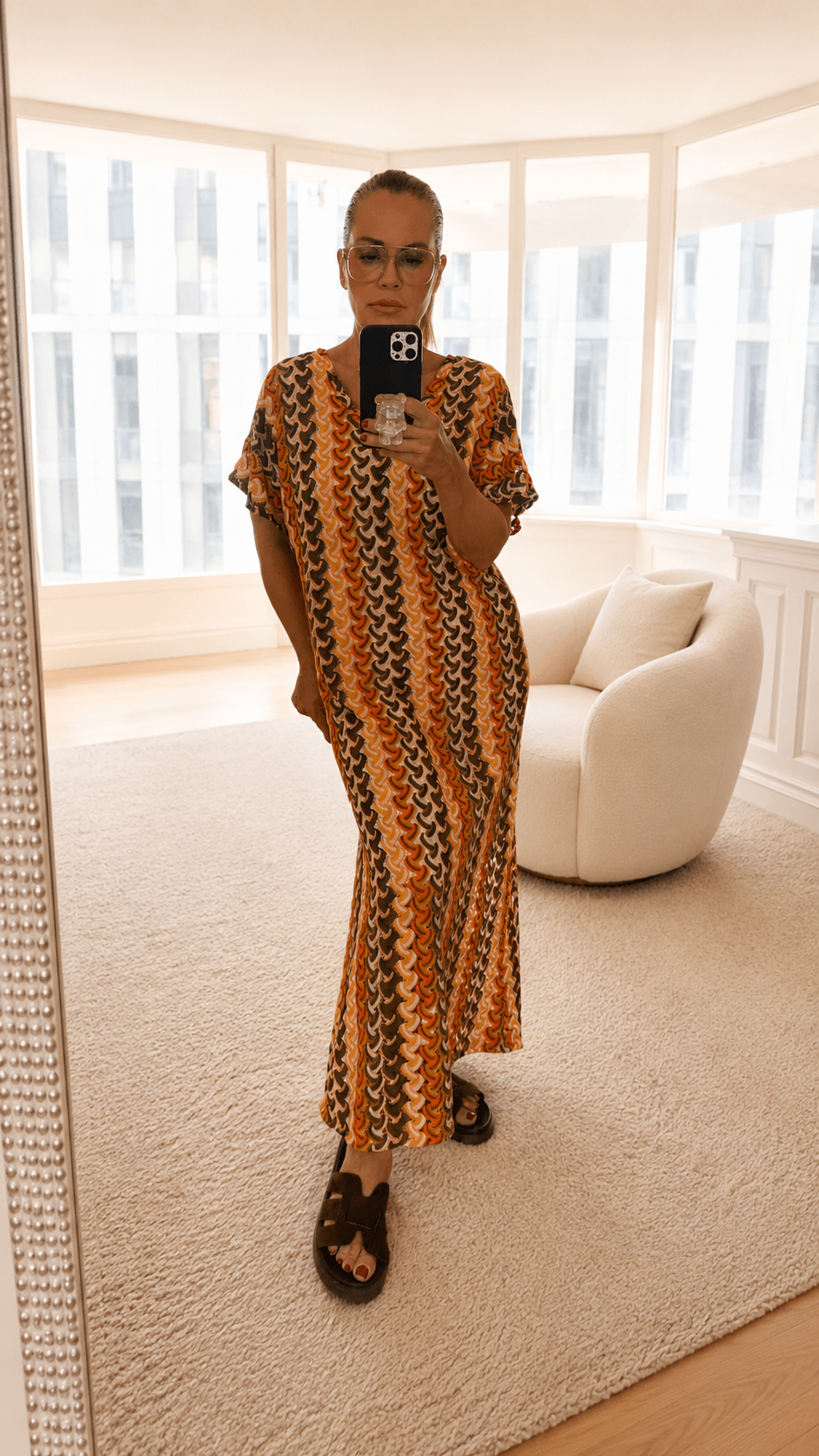 Frau trägt ein langes Sommerkleid mit grafischem Muster in Orange, Braun und Creme. Das locker fallende Kleid hat kurze Ärmel und eine fließende Silhouette.