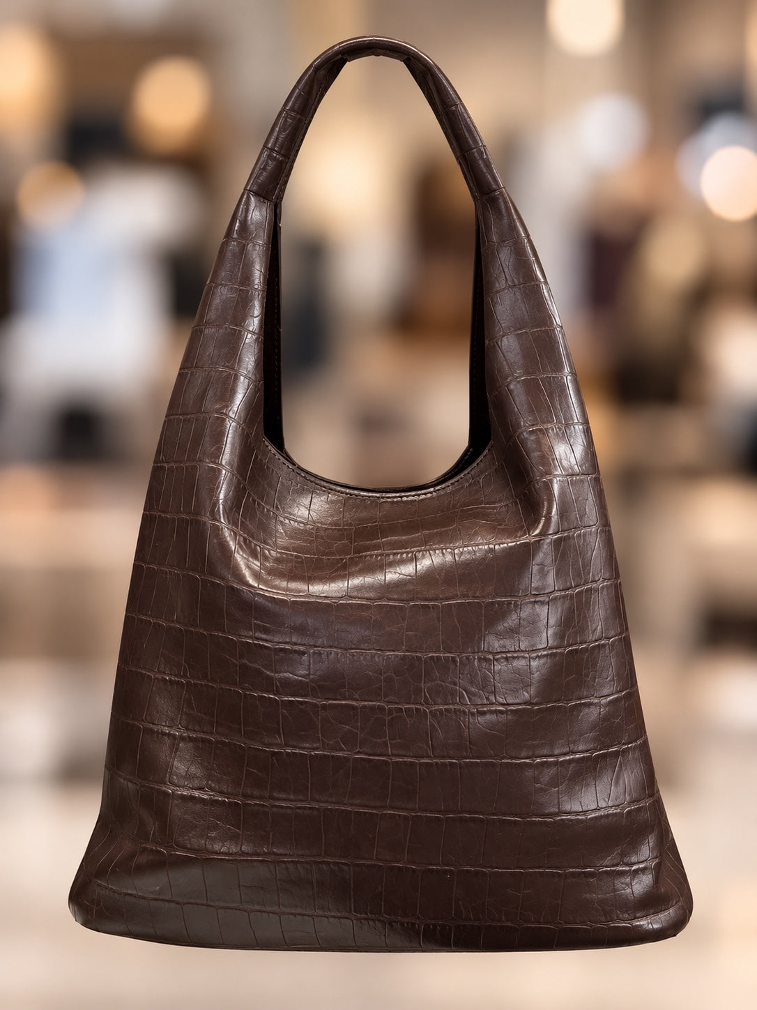 Dunkelbraune Schultertasche mit Kroko-Prägung vor weich verschwommenem Hintergrund