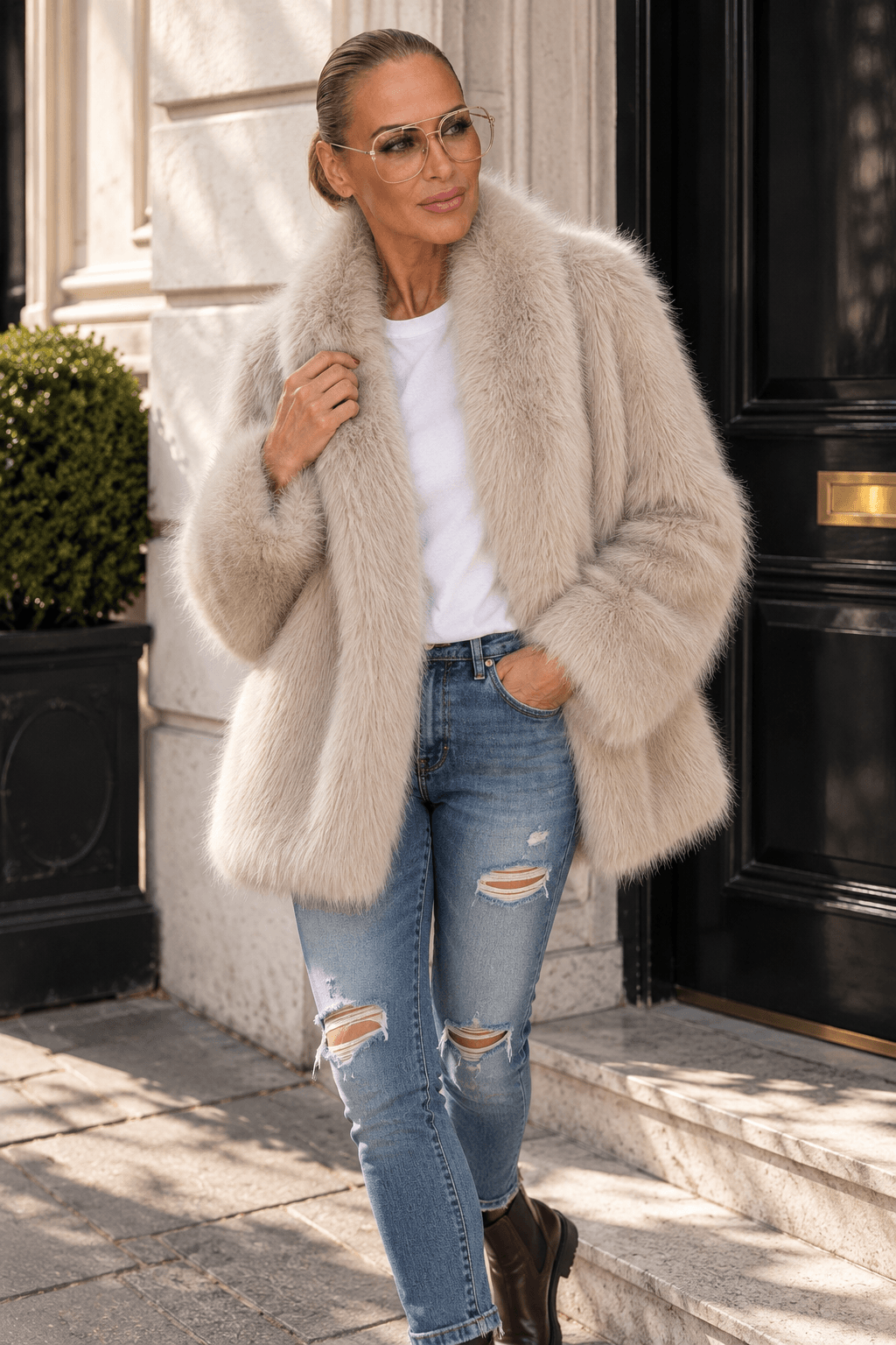 Frau trägt beige Fake-Fur-Jacke mit großem Reverskragen, weißem T-Shirt, Used Jeans und braunen Chelsea Boots.