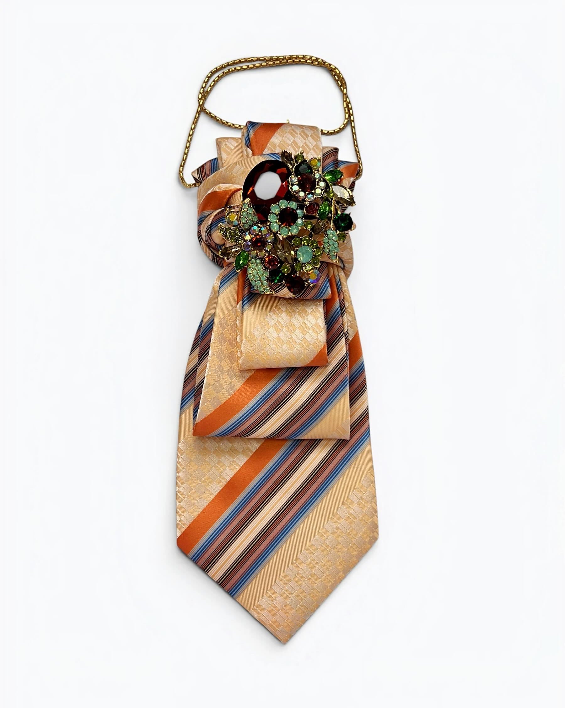 Vintage-Krawatte in Creme, Orange und Blau mit diagonalem Streifenmuster, dekorativer Schmuckbrosche mit bunten Steinen und goldfarbener Kette.